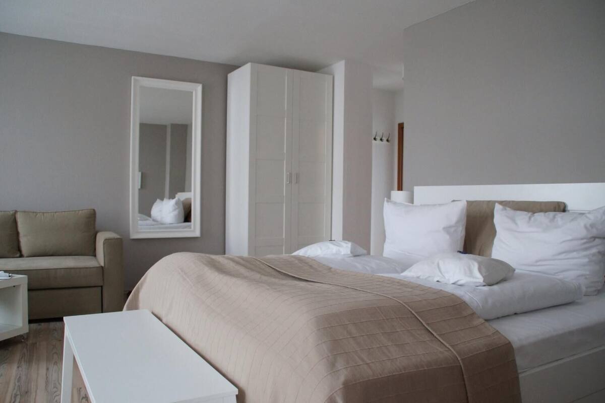 Een moderne hotelkamer met een bed, een stoel, een garderobe en een spiegel.