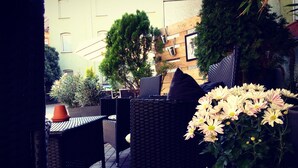 An outdoor seating area with wicker furniture, a potted plant with flowers, and a wooden wall with a picture frame. - Apartment Hotel Lindeneck (Erfurt)
