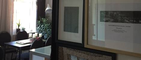 A room with framed artwork on the walls, a dining area with a table and chairs, and a window with curtains.