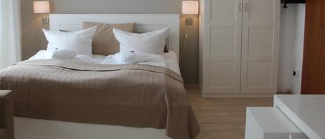 A neatly made bed with a beige bedspread and white pillows, a bedside table with a lamp, and a wardrobe with sliding doors.