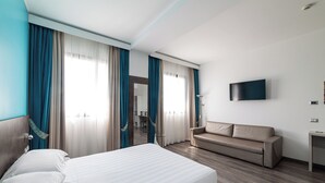 A hotel room with a bed, a sofa, a TV, and a desk. - Phi Hotel Milano (Baranzate)