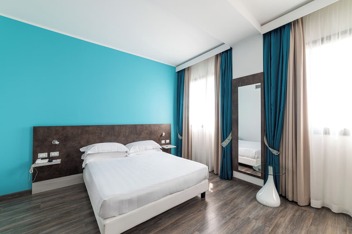 Une chambre d’hôtel moderne avec un grand lit, une table de chevet, un miroir et un vase.
