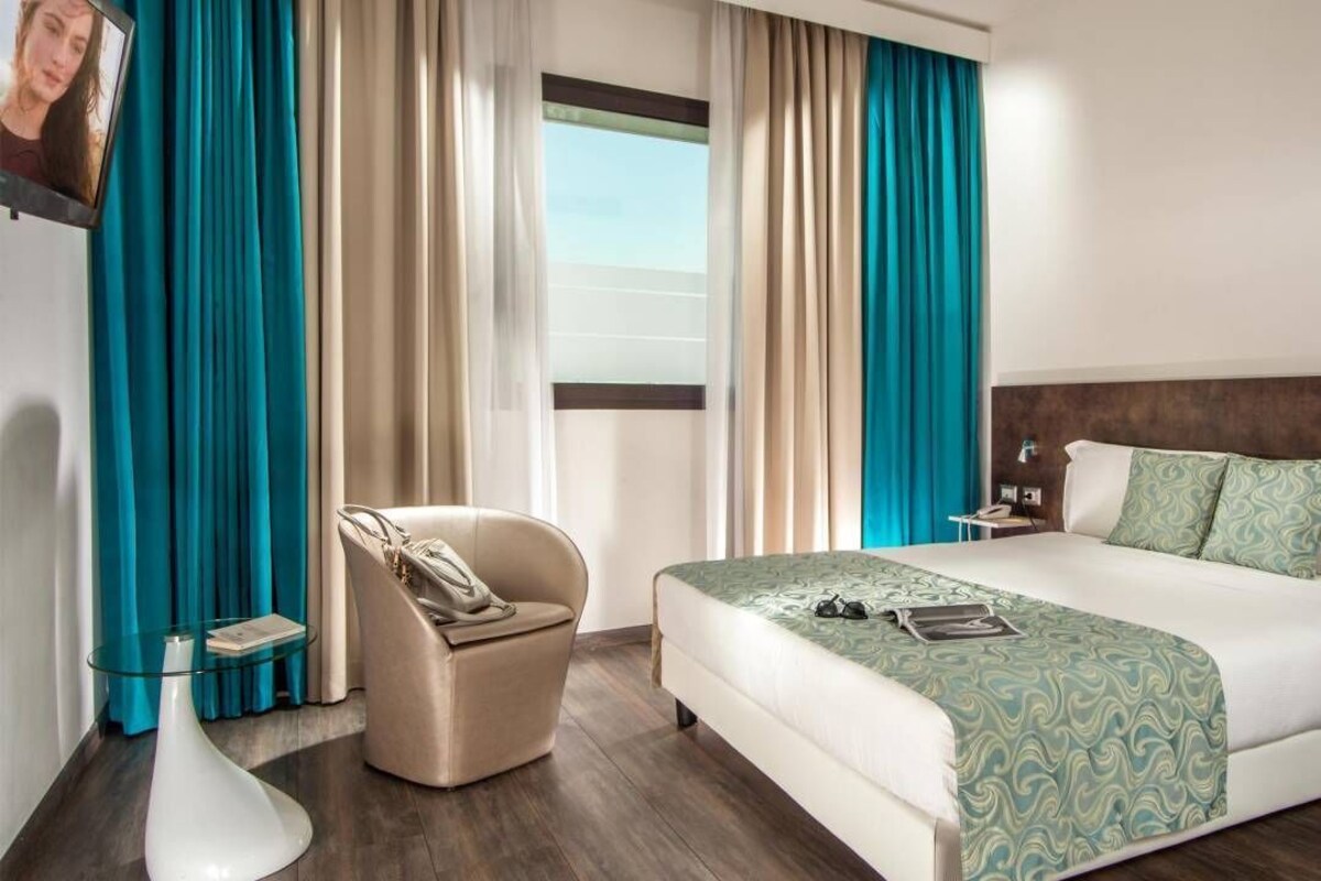 A hotel room with a bed, a chair, a bedside table, a TV, and curtains.