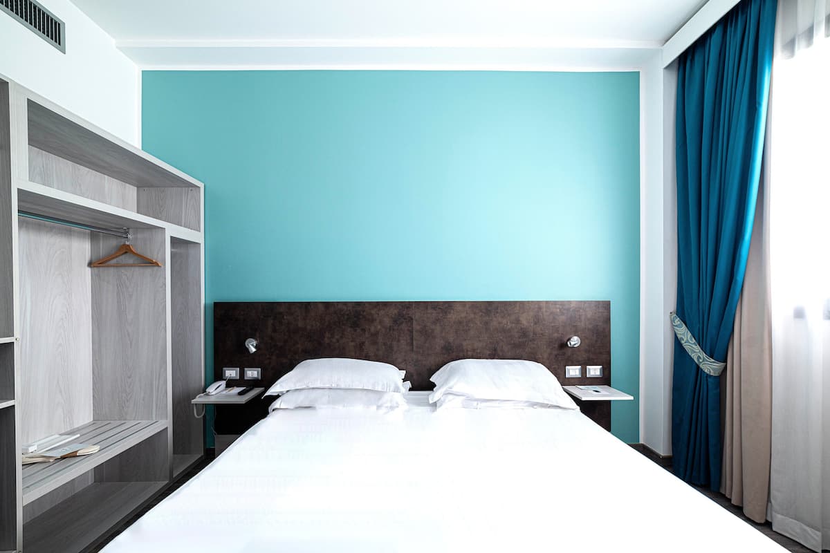Une chambre d’hôtel avec un lit, une armoire, une table de chevet et une fenêtre avec des rideaux.