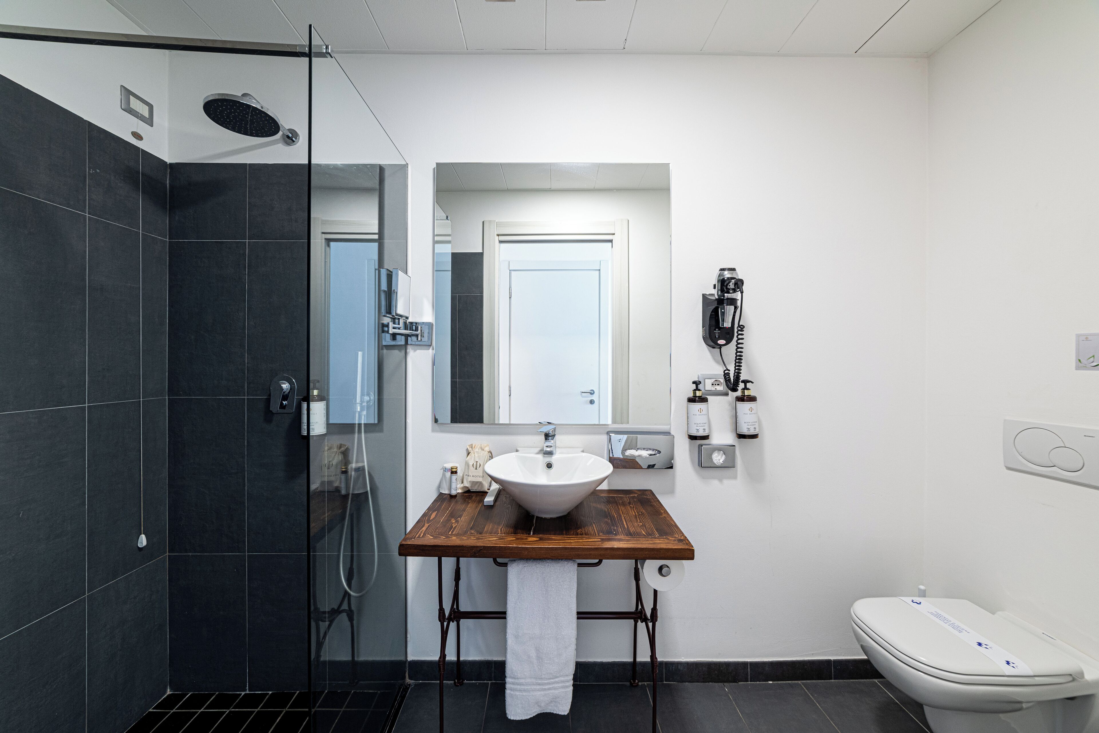 Un baño moderno con tocador de madera, lavamanos blanco, cabina de ducha con mampara de vidrio y un inodoro.
