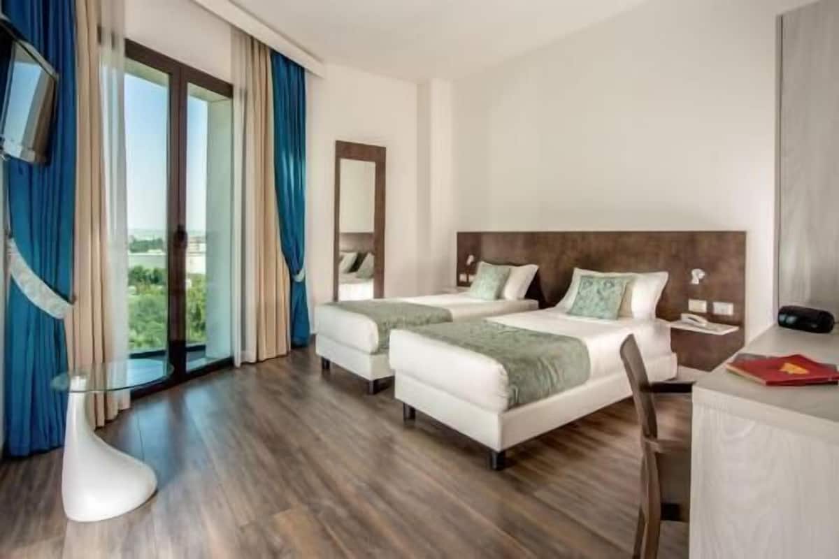 Une chambre d’hôtel avec deux lits, un bureau, une chaise et une grande fenêtre avec des rideaux.