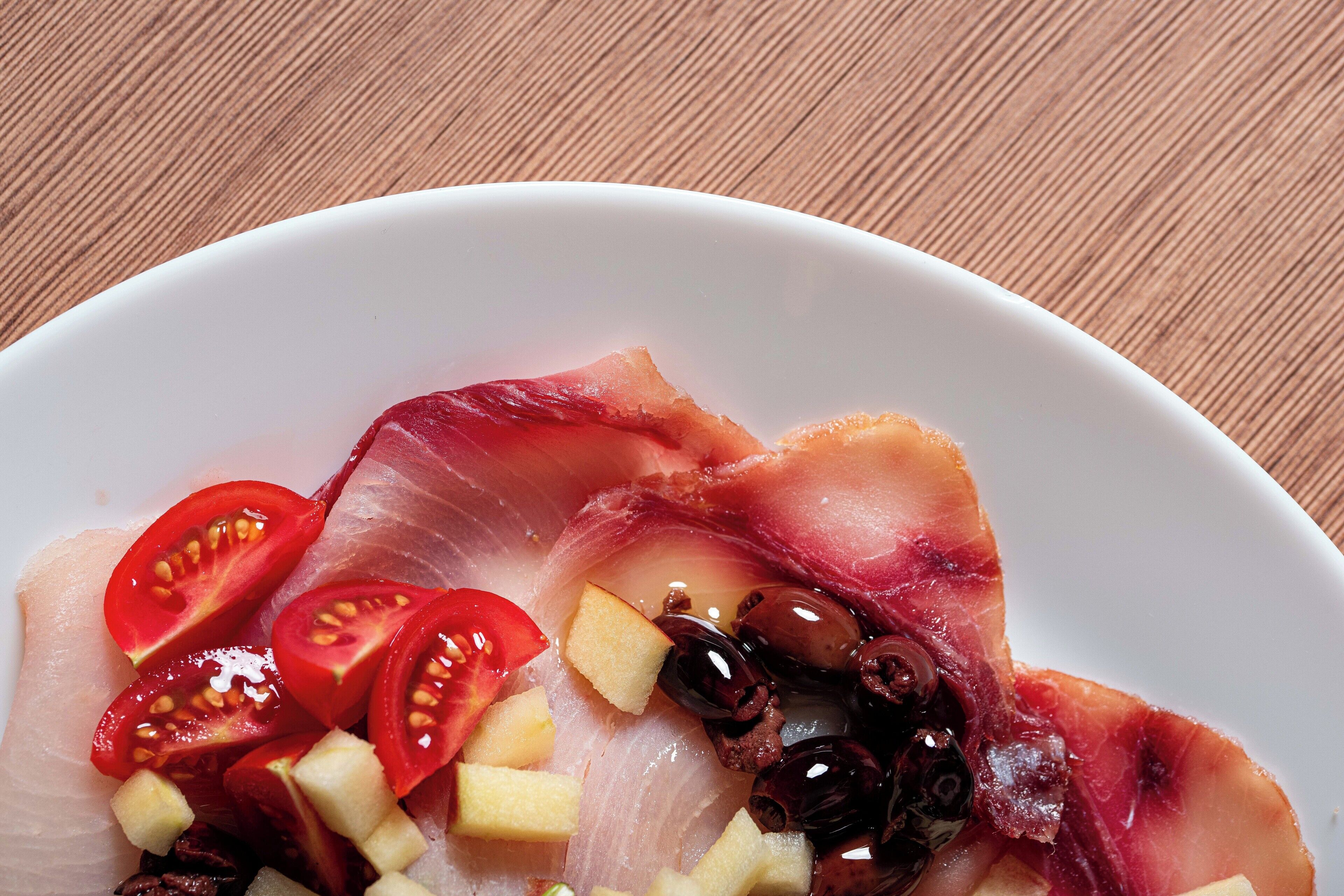 A plate with slices of red meat, cherry tomatoes, and olives.