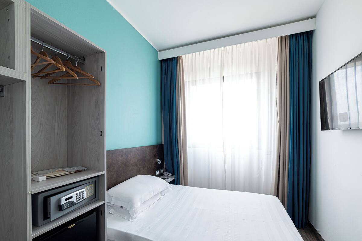 Une chambre d’hôtel avec un lit, une armoire, un bureau et une fenêtre avec des rideaux.