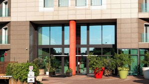 A modern building with a central red pillar, large windows, and potted plants in the entrance area. - Phi Hotel Milano (Baranzate)