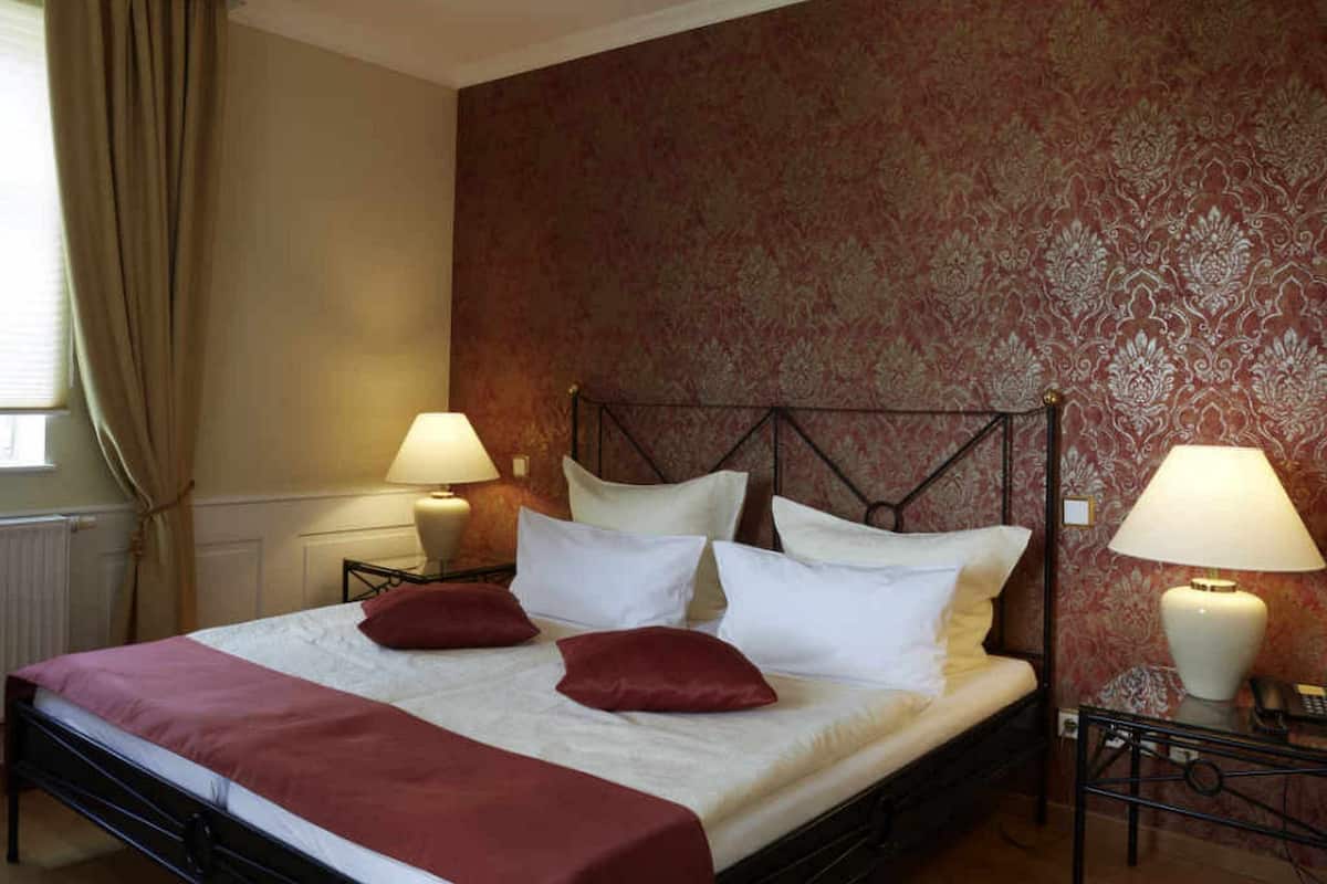 A neatly made bed with white linens and red pillows, flanked by two bedside lamps on matching nightstands.