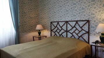 A bedroom with a bed, two bedside tables with lamps, floral wallpaper, and a window with curtains.