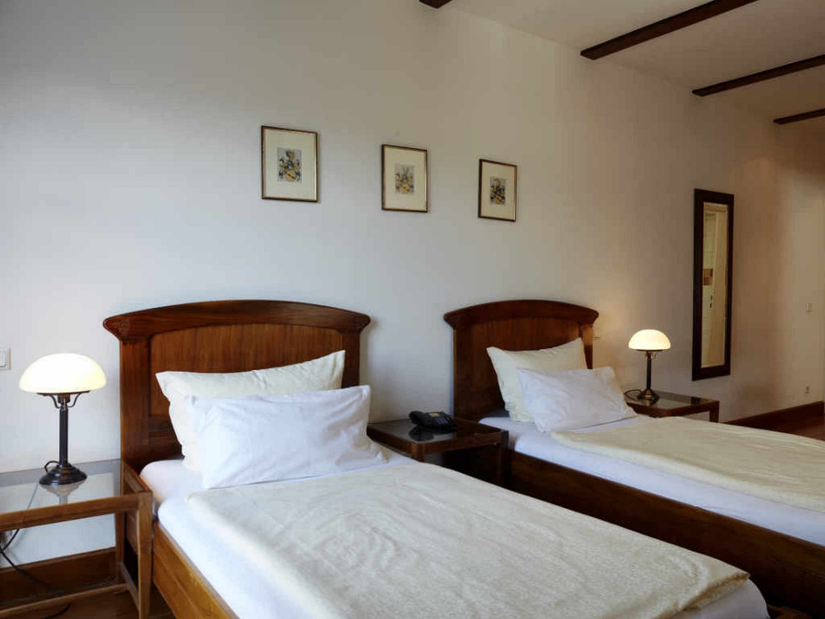 Una habitación de hotel con dos camas individuales, una mesita de noche con lámpara, un teléfono junto a la cama y tres cuadros en la pared.
