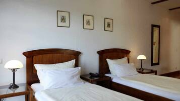 Una habitación de hotel con dos camas individuales, una mesita de noche con lámpara, un teléfono junto a la cama y tres cuadros en la pared.