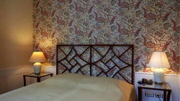 A hotel room with a bed, two bedside tables with lamps, a patterned wallpaper, and a wooden headboard.