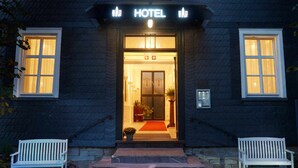 A hotel entrance with a red carpet, two white benches, and a staircase leading up to the door. - Hotel Snorrenburg (Burbach)