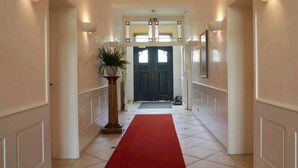 A hallway with a red carpet, a potted plant, a dark door, and a sign above the door. - Hotel Snorrenburg (Burbach)