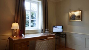 A hotel room with a wooden desk, a chair, a television, and a window with curtains. - Hotel Snorrenburg (Burbach)