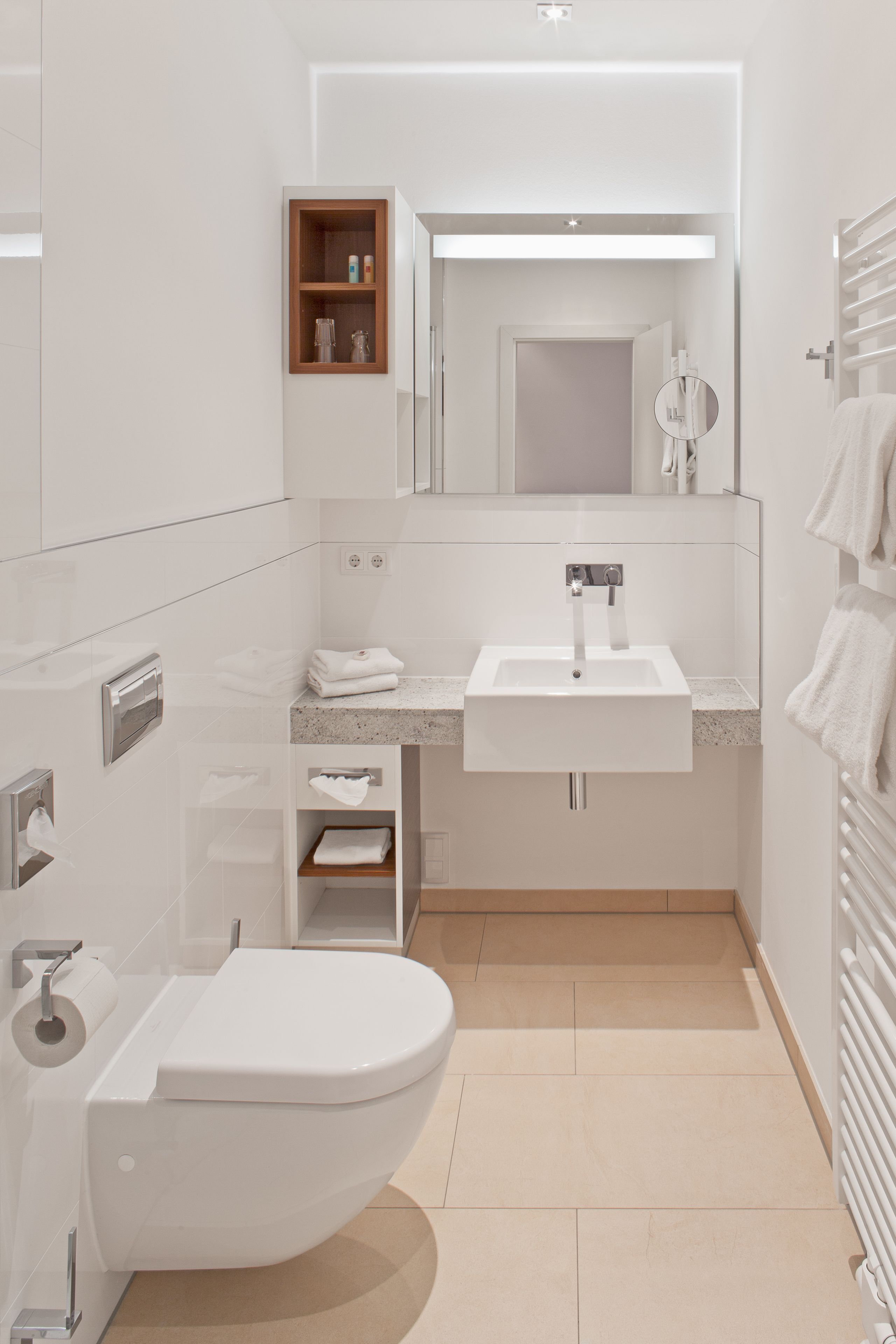 Ein modernes Badezimmer mit einem weißen Waschbecken, einer Toilette, einem Spiegel und einem Handtuchhalter.