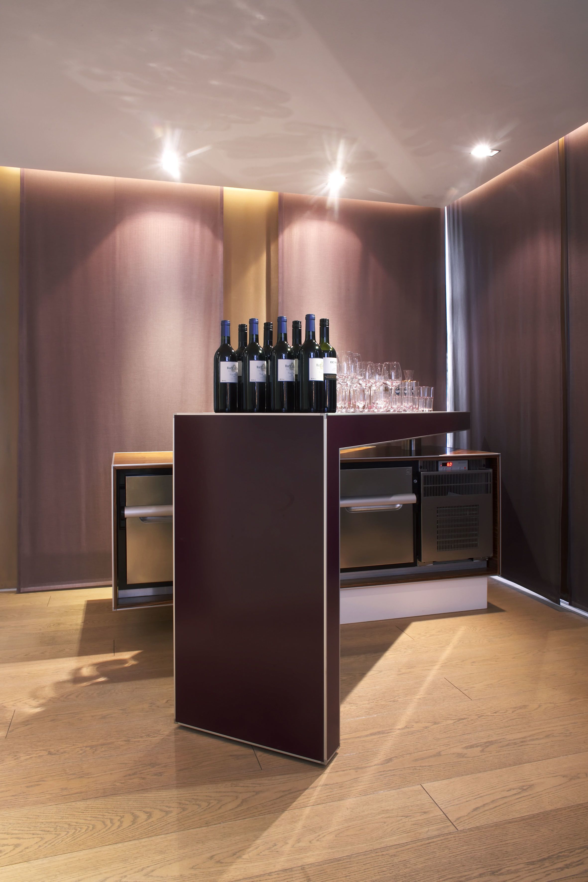A bar area with a wine refrigerator, bottles, and glasses on a shelf.