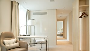 Una habitación de hotel moderna con una butaca de cuero, un escritorio blanco y un vestidor con una percha de madera.