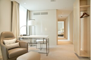 Una habitación de hotel moderna con una butaca de cuero, un escritorio blanco y un vestidor con una percha de madera.