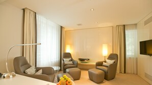Una habitación de hotel moderna con una cama grande, dos sillones, una pequeña mesa con fruta y un televisor en la pared.