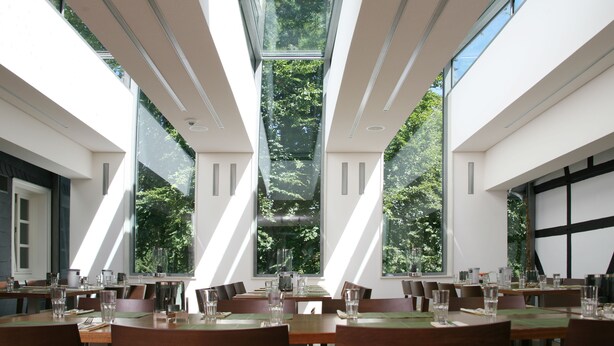 Un comedor moderno con ventanas amplias, varias mesas y sillas dispuestas para comer.