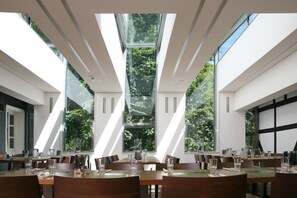 Una zona de menjador moderna amb grans finestres, diverses taules i cadirees disposades per dinar.