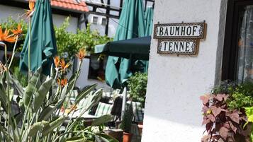 Ein Gebäude mit einem Schild, auf dem "BAUMHOF TENNE" steht, und Außenbestuhlung mit Sonnenschirmen.