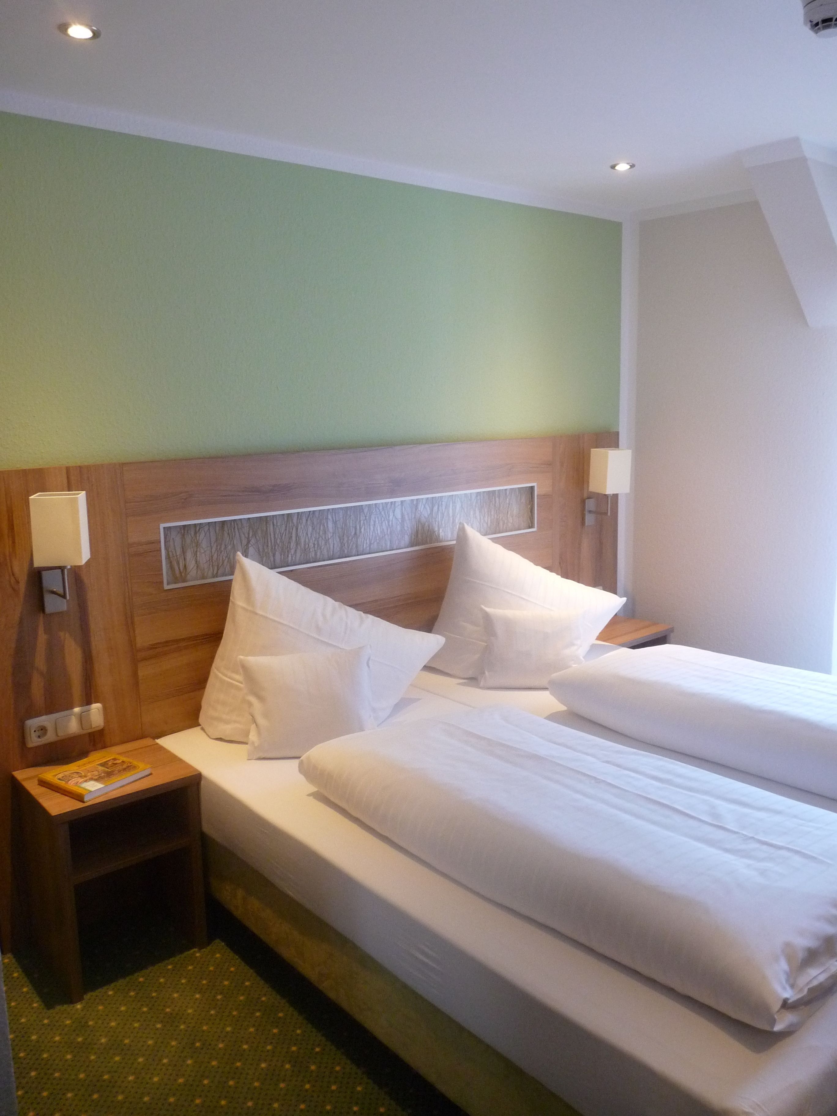 Habitación de hotel con una cama grande, dos mesitas de noche y una lámpara de pared.