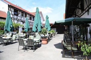 Un café al aire libre con mesas y sillas, sombrillas verdes y plantas en macetas.