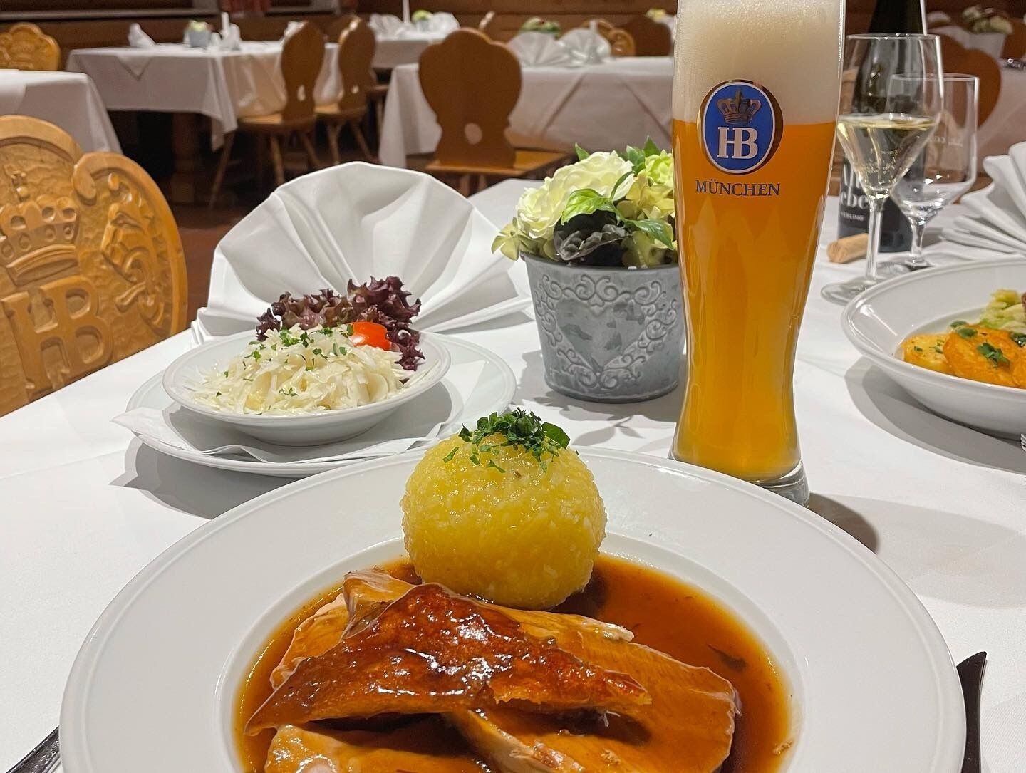 A dining table with a plate of food, a glass of beer, and a bowl of salad.