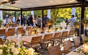 Un área de comedor al aire libre con mesas dispuestas para los comensales, rodeada de follaje y árboles.