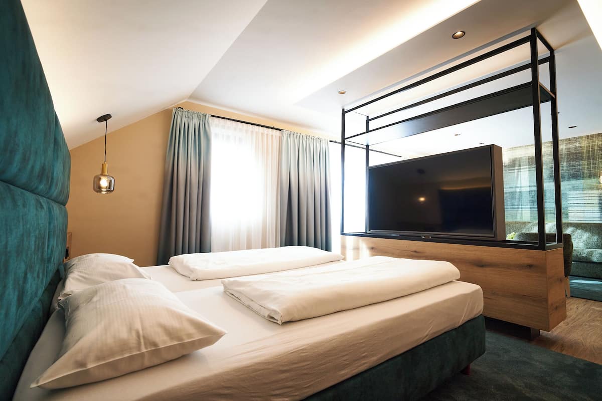 A modern hotel room with a bed, a TV, and a window with curtains.