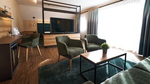 En moderne stue med et fjernsyn, to lænestole, et sofabord og et køkkenområde med bordplade og vask.