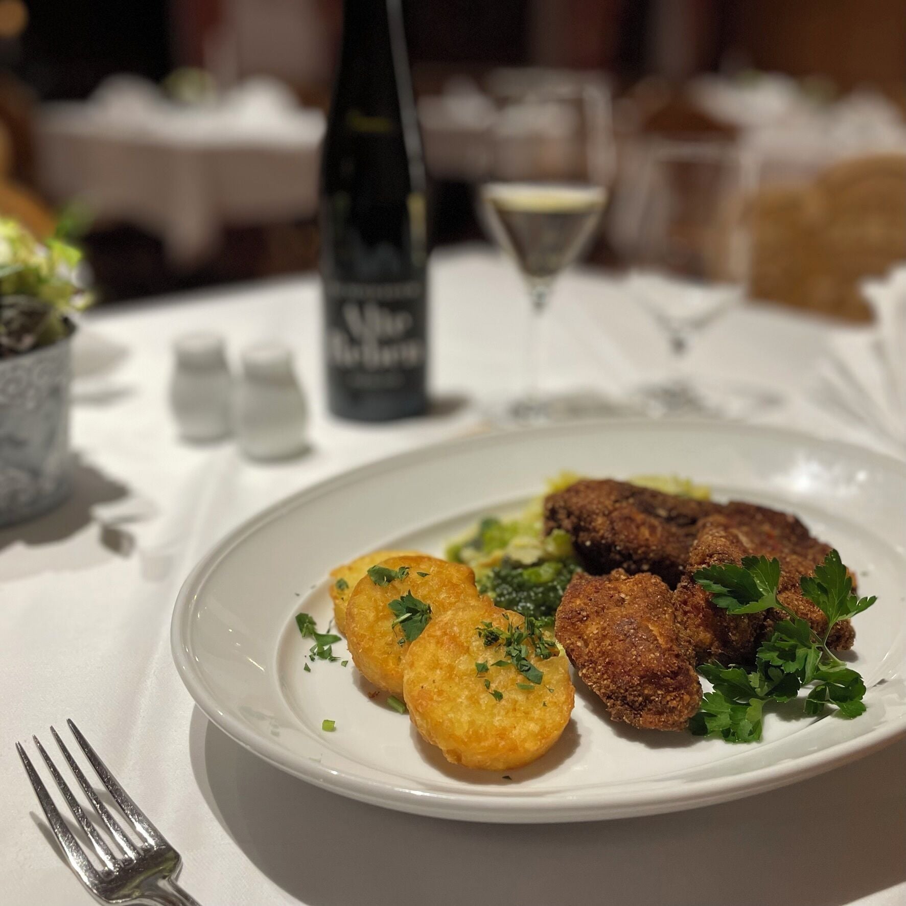 Ein Teller mit Essen, eine Gabel daneben, eine Flasche und ein Glas im Hintergrund.