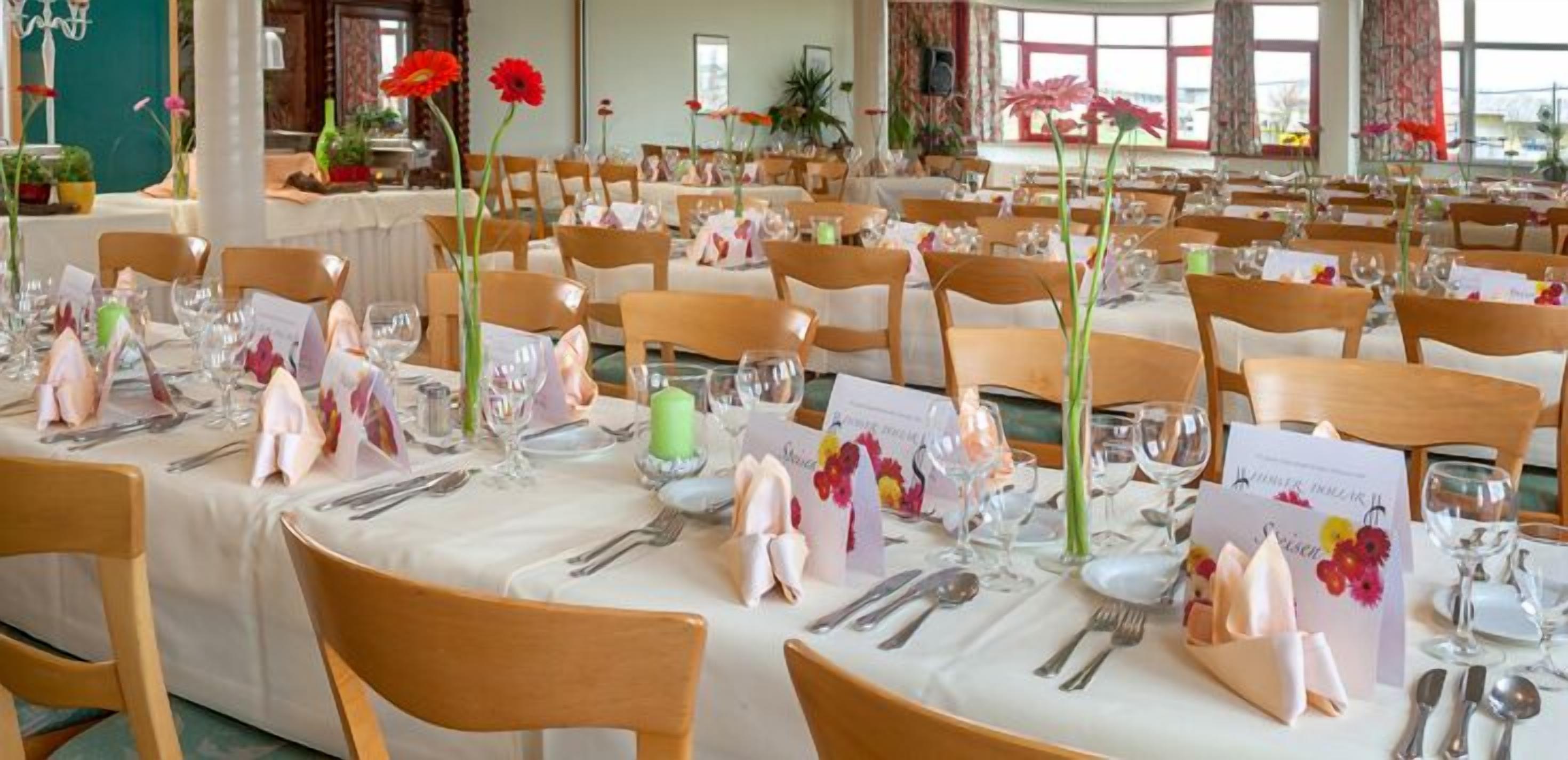 Uma sala de banquetes com várias mesas montadas para um evento formal, cada uma com louça, copos e arranjos florais.