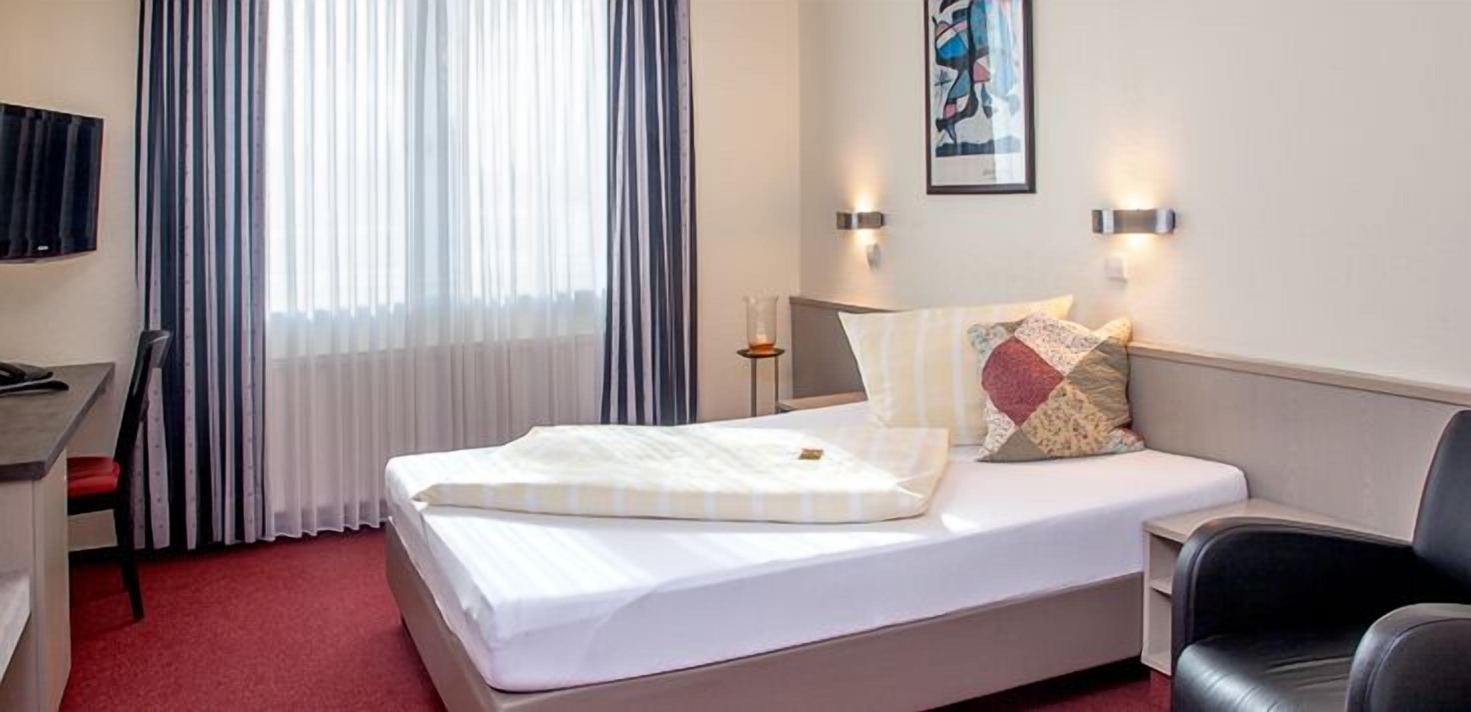 Habitación de hotel con cama, escritorio, silla y televisor.