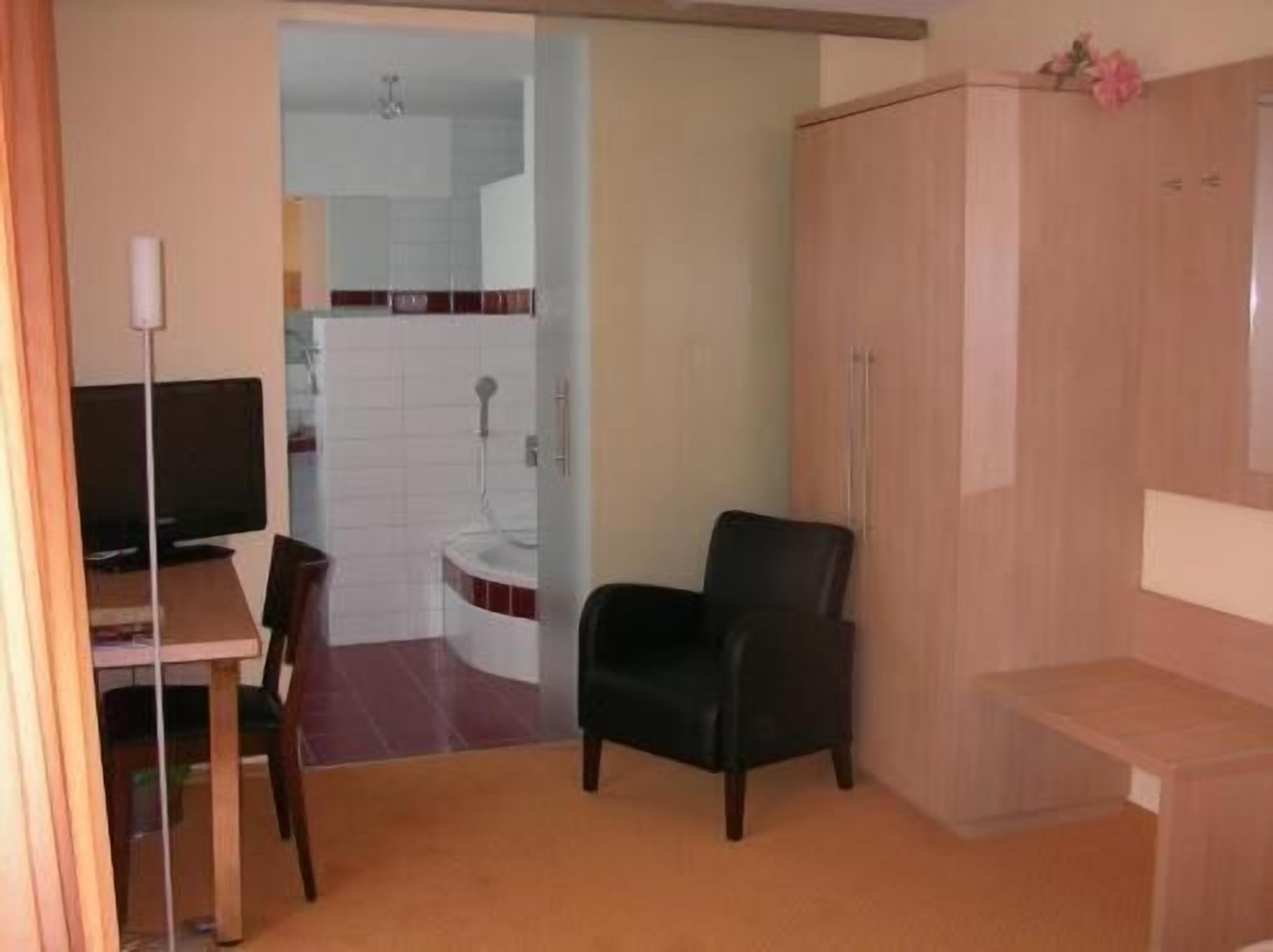 A small room with a desk, a chair, a wardrobe, and a bathroom visible through an open door.