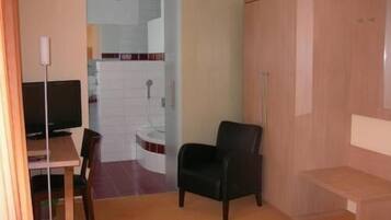 A small room with a desk, a chair, a wardrobe, and a bathroom visible through an open door.