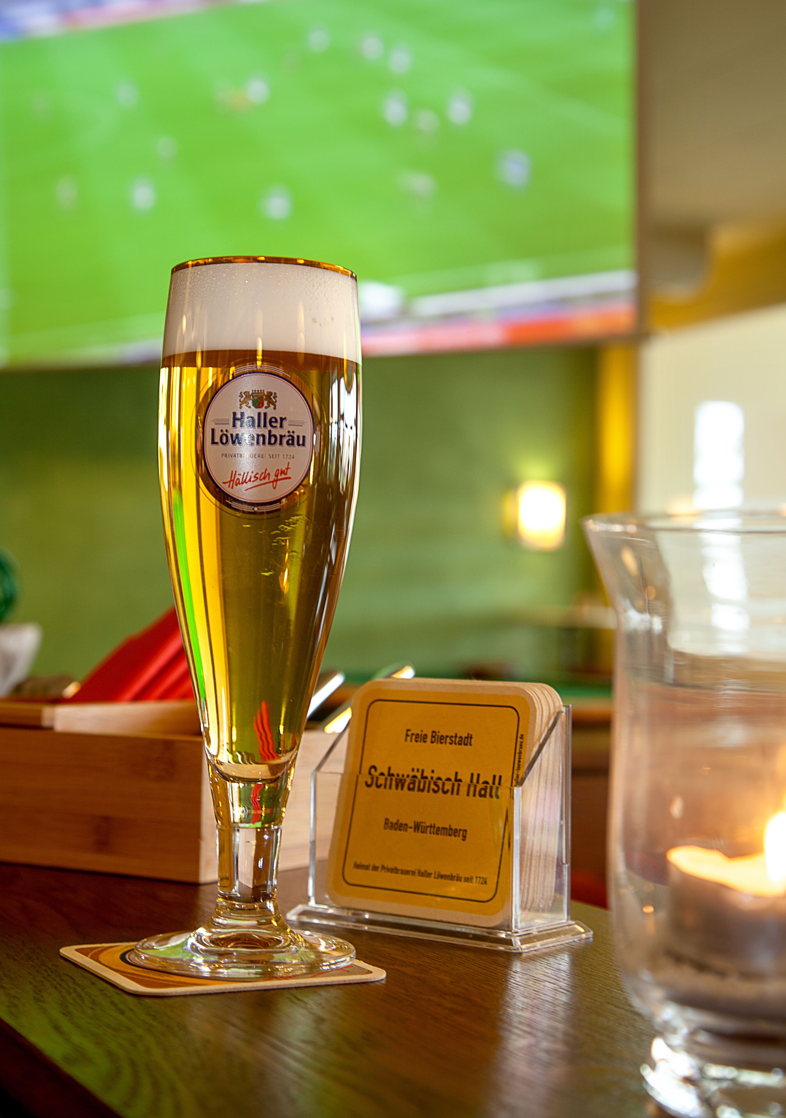 A glass of beer with a label, a candle, and a sign on a table.