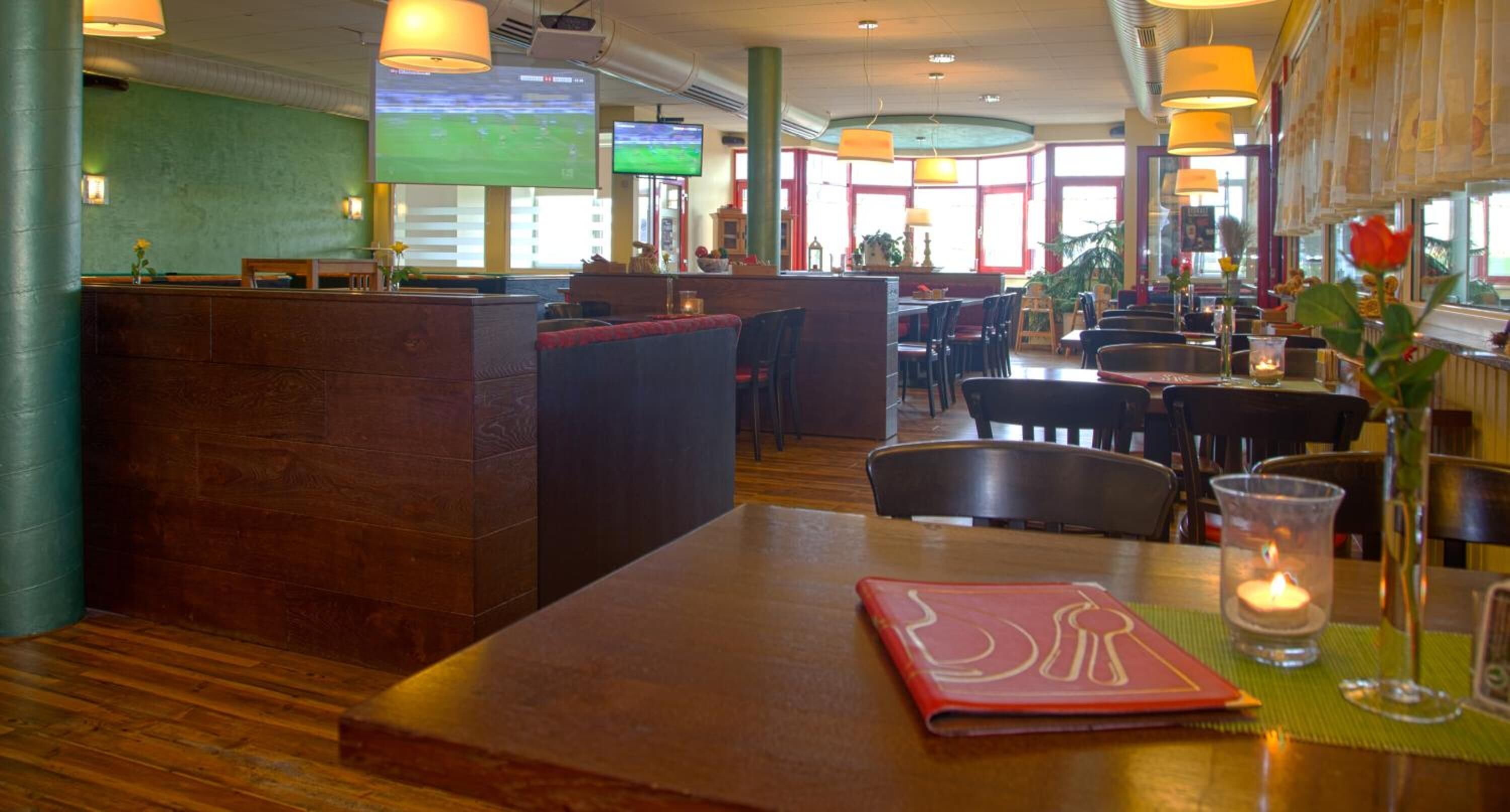 A restaurant with wooden tables, a bar area, and a TV screen displaying a sports game.