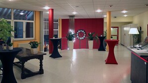 A lobby with a red wall, a clock, potted plants, and a reception desk. - Sporthotel Öhringen (Öhringen)