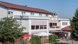 A two-story building with a red roof, a sign for a restaurant, and outdoor seating with umbrellas. - Sporthotel Öhringen (Öhringen)