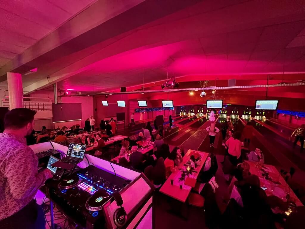 A bowling alley with multiple lanes, a DJ booth, and people playing.
