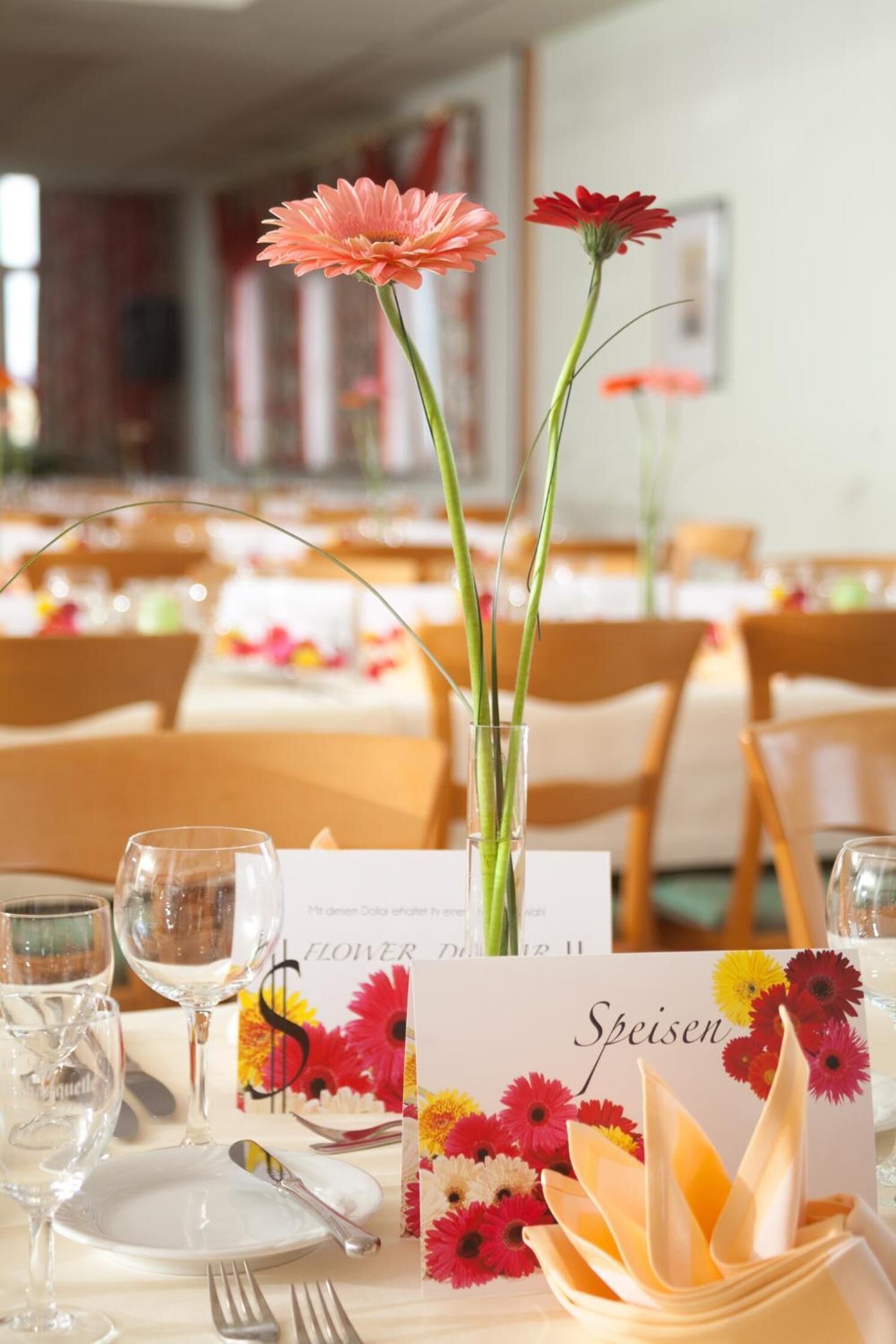 Ein Esstisch ist gedeckt mit einer Speisekarte, Weingläsern und einer Blumenvase.