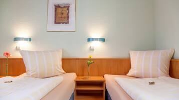 Una habitación de hotel con dos camas, cada una con un cojín y una mesita de noche. Hay un cuadro enmarcado en la pared sobre las camas.