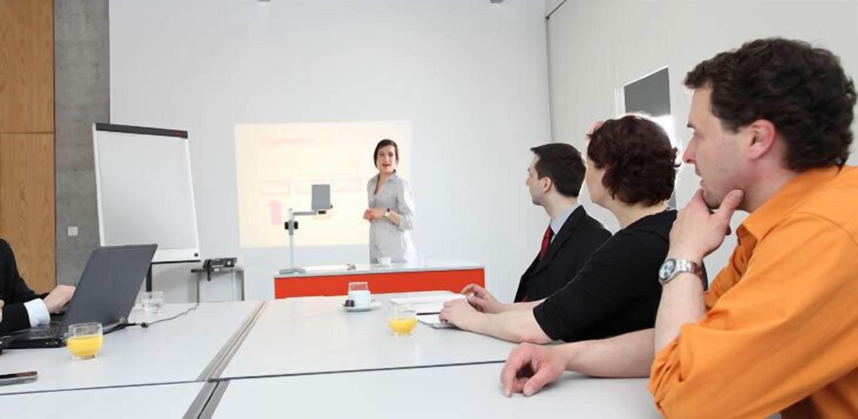 A conference room with a presentation screen, a whiteboard, and a table with laptops and cups.