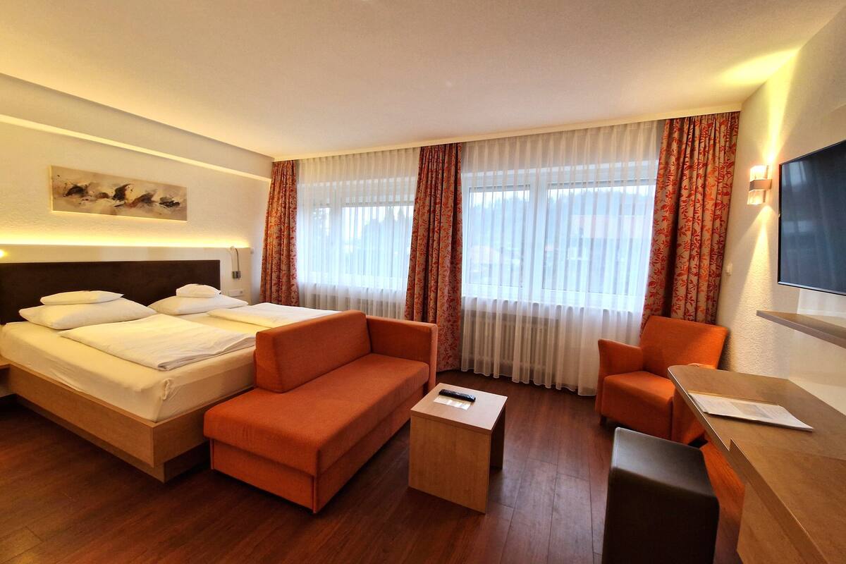 Una habitación de hotel con una cama, dos sofás naranja, una mesita de madera y un televisor.