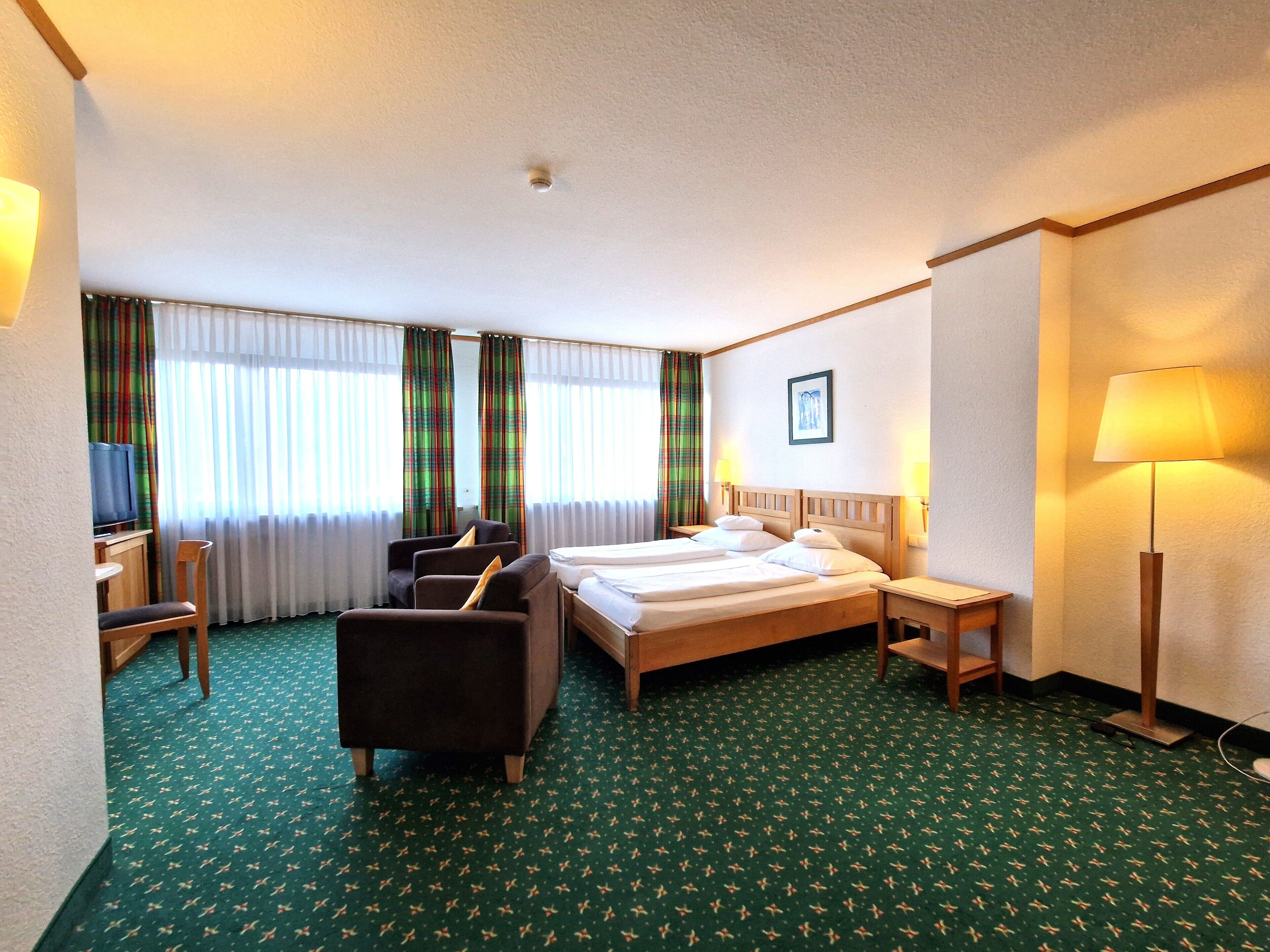 A hotel room with a bed, two chairs, a desk, a TV, and a lamp.